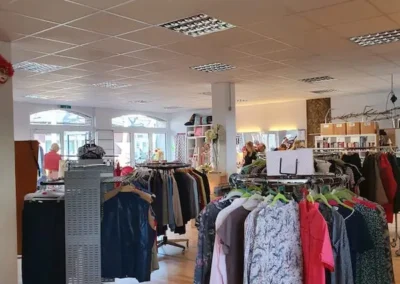 Blick in die Bekleidungsabteilung eines Secondhand-Ladens mit diversen Kleidungsteilen auf Kleiderständern und Regalen.